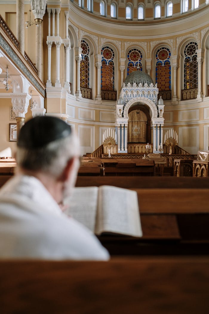 Jewish man reads Torah inside an ornate synagogue, emphasizing tradition and worship in a sacred space.