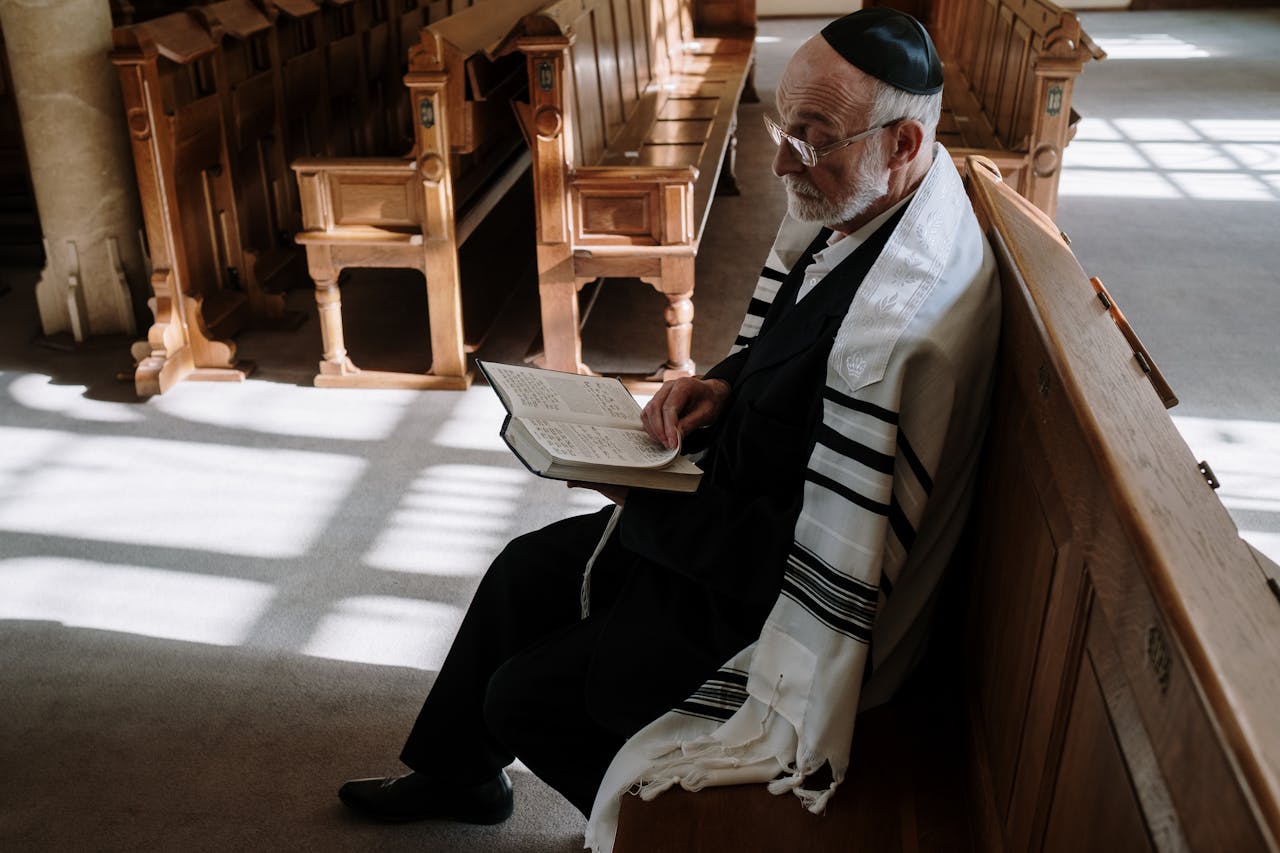 mobile-02 Elderly man wearing kippah and tallit, reading in a synagogue. Traditional Jewish setting.