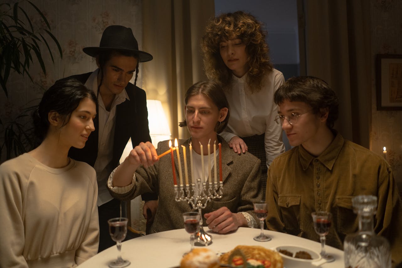 A group of young adults celebrating Hanukkah by lighting a menorah indoors.
