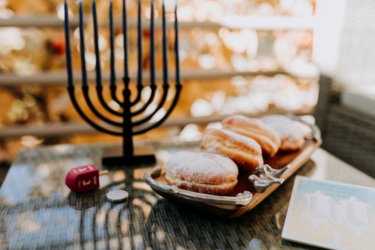 mobile-01 A vibrant Hanukkah scene with a menorah, dreidel, and sufganiyot on a reflective surface.