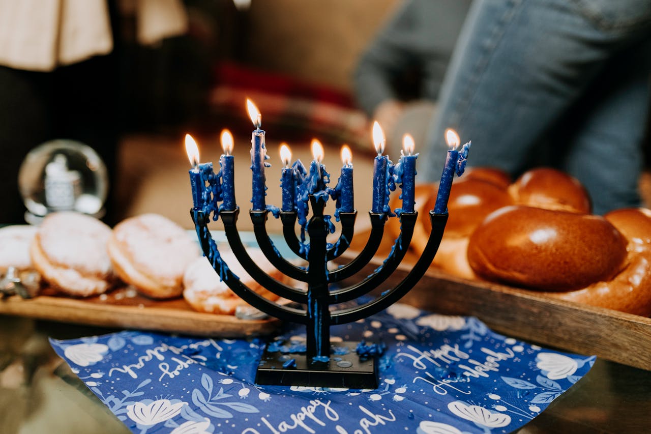 creative-03 Lit menorah on a festive Hanukkah table with traditional foods like challah and sufganiyot.